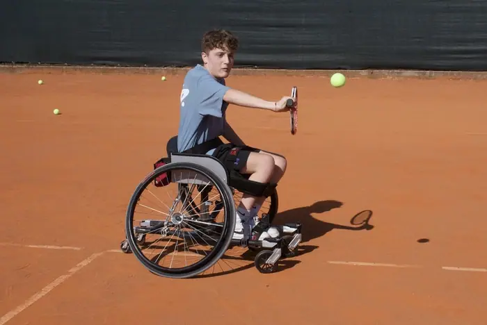 Giovane tennista in carrozzina su terra rossa.